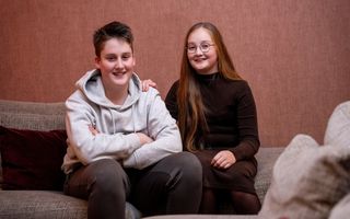 Jongen in grijze hoodie en meisje met lang haar en bril zitten samen op een bank.