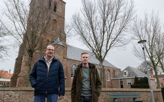 Man op leeftijd met blauwe jas en jonge man met bruine jas voor een oud kerkje.