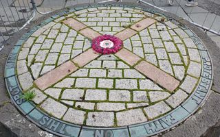 Binnen een cirkel van klinkers ligt een gedenksteen met een roze krans eromheen. 