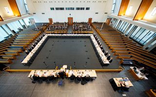 Luchtfoto van vergadertafels in een modern kerkgebouw; om de tafels zitten veertig mannen in zwarte pakken.