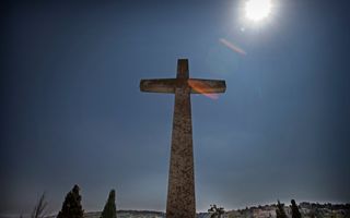 Stenen kruispaal tegen blauwe lucht met op de achtergrond een stad.