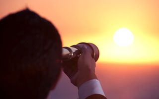 Een persoon kijkt door een verrekijker naar de zonsopgang.