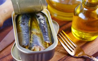 Een bakje met vis in olie. Rechts potjes olie en een vork. 