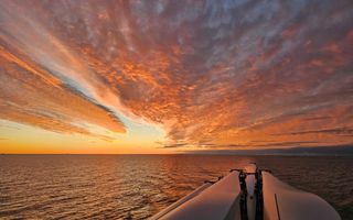 Oranje lucht boven water, op de voorgrond een deel van een schip.