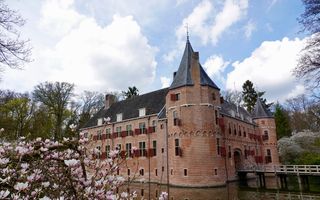 Kasteel met rode luiken, omringd door gracht en daarnaast bloemen en kale bomen.