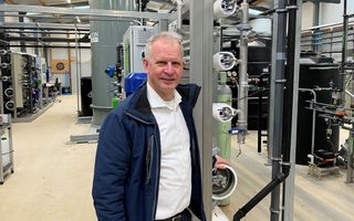 Een glimlachende man staat voor een technische installatie van buizen, vaten en kokers.  