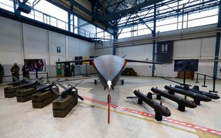 Defensiemateriaal in een grote bedrijfshal. In het midden een soort klein vliegtuig, aan weerszijden ervan projectielen.