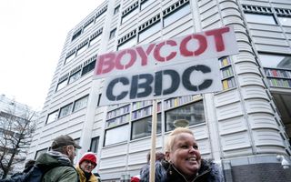 Vrouw met kort blond haar houdt bord omhoog met de tekst ”Boycot CBDC”. Ze protesteert tegen de digitale euro. 