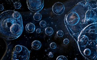 Foto die sterk is ingezoomd op zwart ijs met luchtbubbels die witte kringen vormen in het beeld.