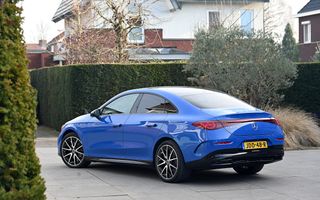 Een blauwe auto staat op een grijze tegelondergrond. Op de achtergrond een groene heg en wat struiken.