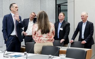 Groepje mannen en vrouw in nette kleding overleggen met elkaar. 