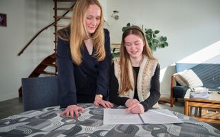 Twee meiden staan gebogen over een profielwerkstuk dat op tafel ligt.