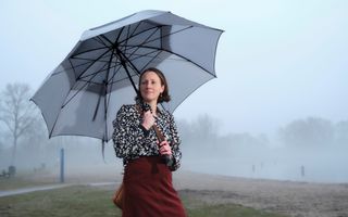 Vrouw in rode rok en gebloemde blouse houdt paraplu vast en is gefotografeerd tegen mistige achtergrond.