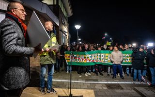 Man in dikke jas houdt plaat omhoog die hij kreeg van demonstanten met spandoek.