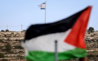 Een zwart-wit-groen-rode Palestijnse vlag wappert op de voorgrond, met op de achtergrond een gehavende blauw-witte Israëlische vlag.