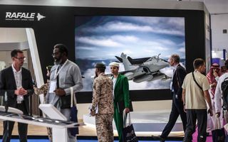 Mensen lopen langs afbeelding van gevechtsvliegtuig op beurs.