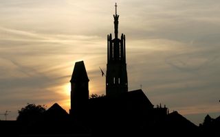 Zwart silhouet van de toren van de Sint-Willibrorduskerk in Huls bij zonsondergang.