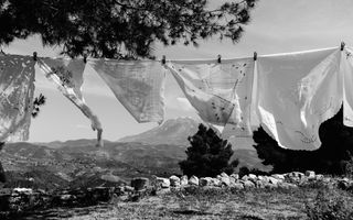 Aan een waslijn hangen witte doeken te wapperen in een berglandschap. De foto is zwart-wit.