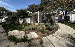 Wit huis met veranda, omgeven door bomen en struiken.