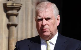 Een man met grijs haar in pak knijpt zijn ogen bijna dicht tegen de zon. 