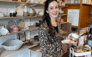 Jonge vrouw met donker haar in een pottenbakkersatelier, met verschillende gebruiksvoorwerpen die ze maakt.