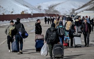 Mensen lopen met koffers en tassen over asfaltweg.