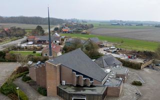Luchtfoto van een modern kerkgebouw met een ranke torenspits. Op de achtergond landbouwgrond.
