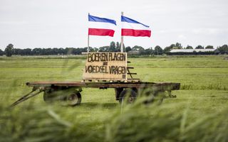 Op een weiland staat een platte kar met daarop twee omgekeerde Nederlandse vlaggen en een bord met de tekst: Boeren plagen = voedsel vragen.