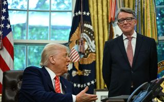 Man in donker pak achter bureau spreekt met man in donker pak en bril op die naast het bureau staat.