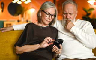 Een man en vrouw zitten samen op de bank en kijken bedachtzaam naar het scherm van een smartphone.