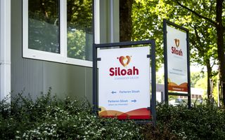 Bord met het logo van Siloah, zorggroep Sirjon, staat in de struiken bij een gebouw.