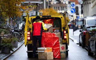 Een bezorger laadt pakketjes uit zijn bus bij een pakketpunt van DHL.