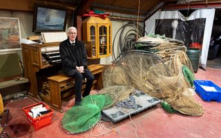 Man in een zwart pak op een orgelbank op een nettenzolder.
