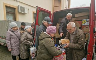 Oudere vrouwen met jassen en mutsen aan staan bij rode bus waar twee mannen broden uitdelen.