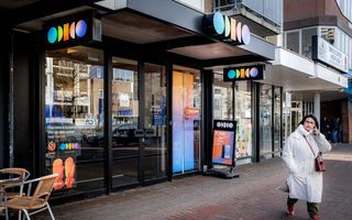 Een vrouw in witte jas loopt bij een Odido-winkel.