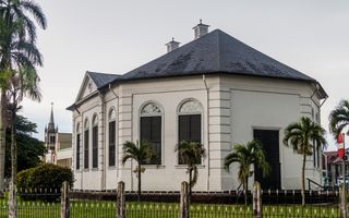 Achthoekig, wit kerkgebouw met palmbomen eromheen. Op de achtergrond is de toren van een andere kerk te zien.