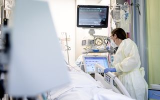 Een vrouw in beschermende kleding kijkt naar een monitor. Links van haar ligt een patiënt in bed. 