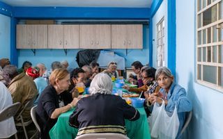 Oudere mannen en vrouwen eten gezamenlijk aan lange tafels.
