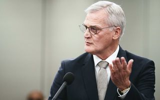 Een man in pak gebaart met zijn hand en spreekt in een microfoon.