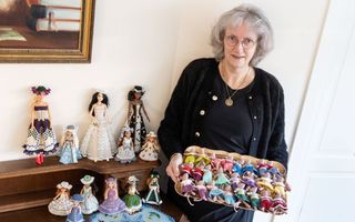 Mevrouw in zwarte kleding houdt dienblad vast met muisjes gemaakt van kralenwerk. Naast haar nog meer werkstukken. 