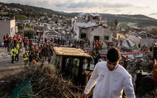 Mensen met oranjes en gele hesjes aan staan bij puinhopen van gebouw dat door raket is getroffen.
