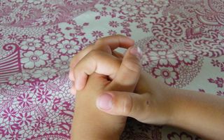 Twee gevouwen kinderhanden rusten op een paars-wit tafelkleed.