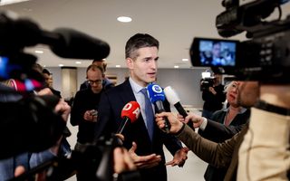 Man in pak met om hem heen journalisten met microfoons en camera’s.