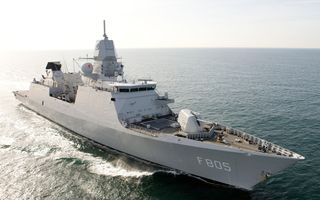 Een grijs schip met een groot kanon op de boeg vaart op zee.