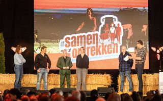 Mensen staan op een podium met achter hen strobalen. 