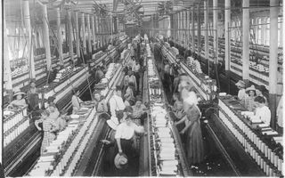 Zwart-witfoto van een fabriekshal waarin mensen werken bij spinmachines.