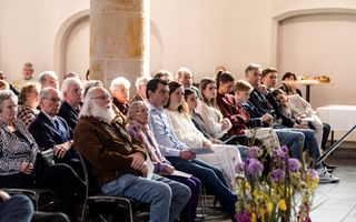Mensen zitten op stoelen in een oude kerk met witte muren.