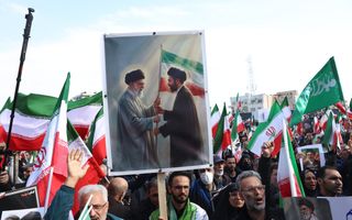 Mensen zwaaien met groen-wit-rode vlaggen en houden een bord vast met twee mannen die een vlag aan elkaar overgeven. 