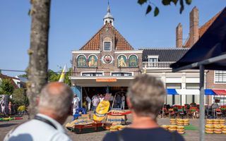 Langs twee hoofden van toeristen kijk je op de kaasmarkt in Edam. Vanuit het waaggebouw worden de kazen verhandeld.