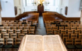 Een opengeslagen Bijbel op de kansel in een kerk gevuld met stoelen.